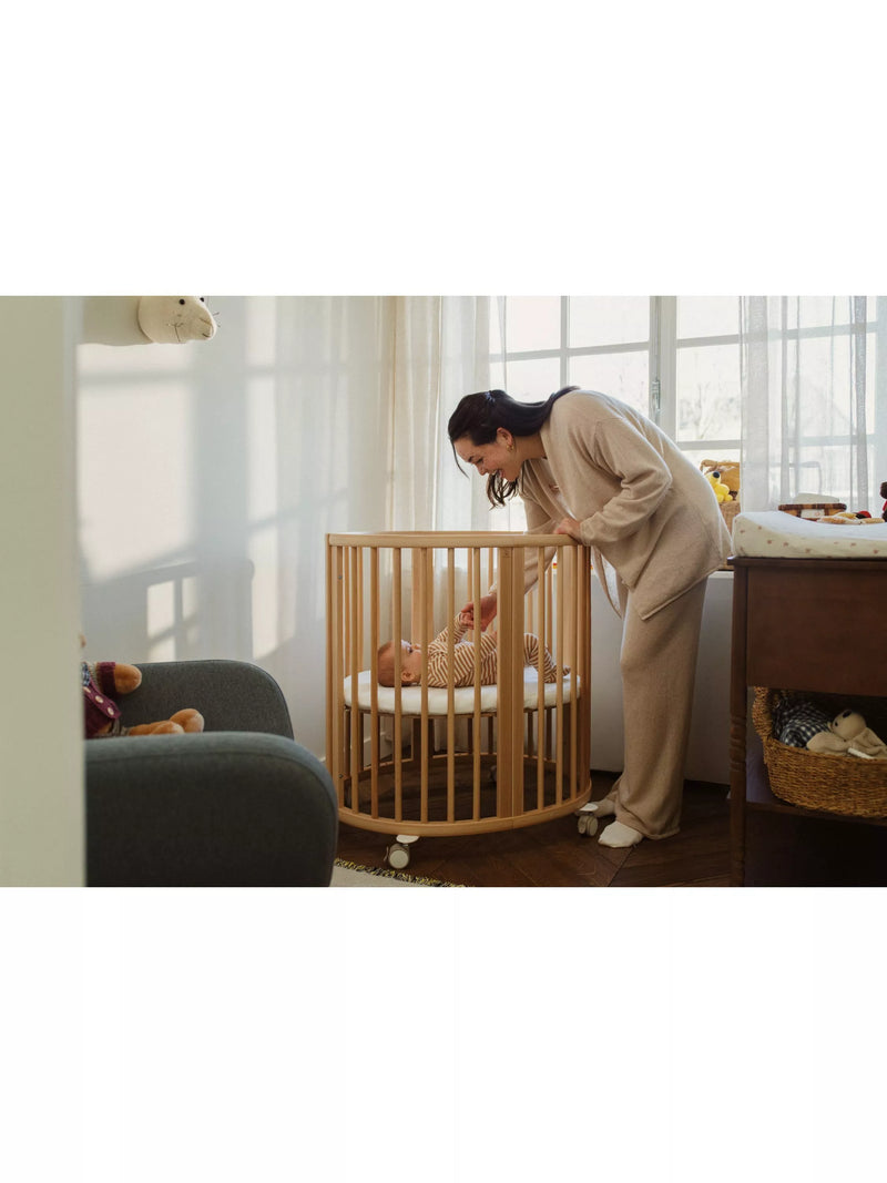 Stokke mini oval crib with natural finish, adjustable height, and wheels (British brand)
